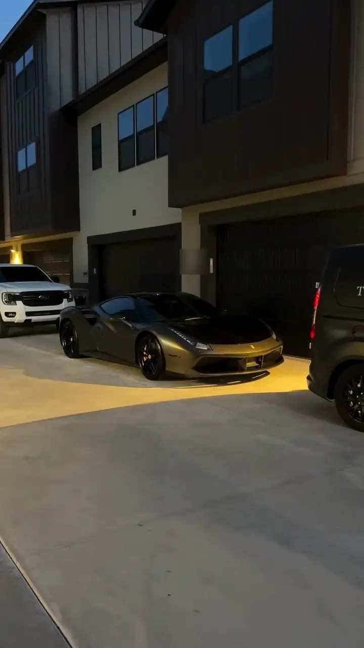 A dark Ferrari at dusk outside a modern home