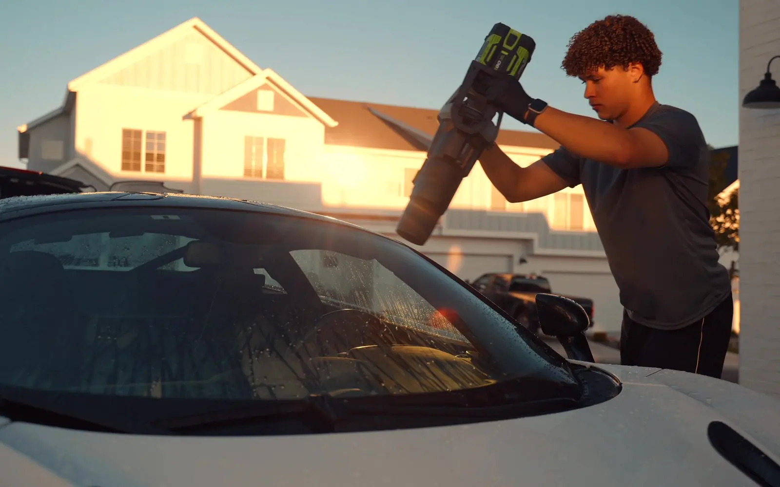 A detailer drying the windshield of a white McLaren 720S at golden hour