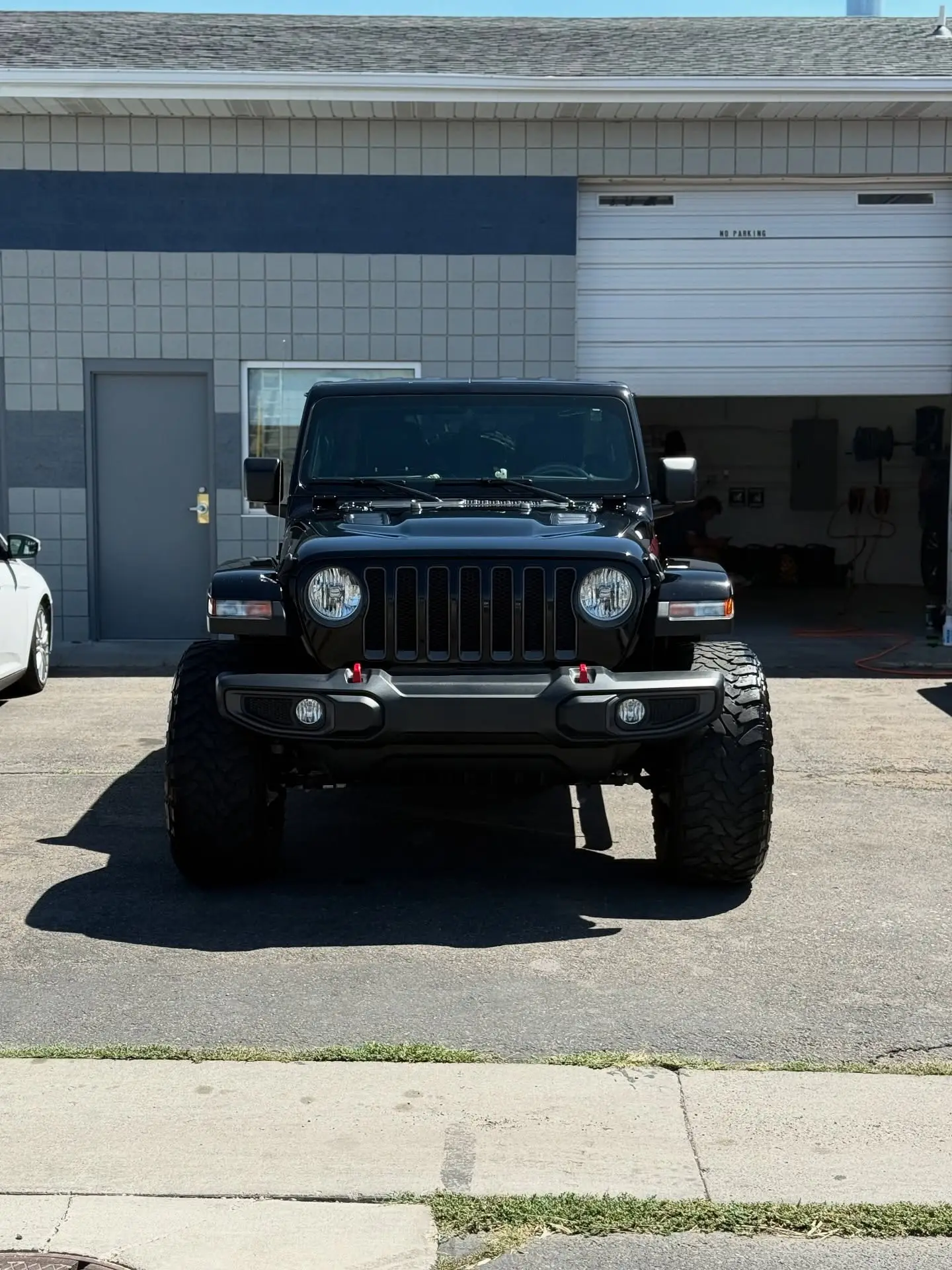 A black Jeep Wrangler parked square in front of the open shop bay door