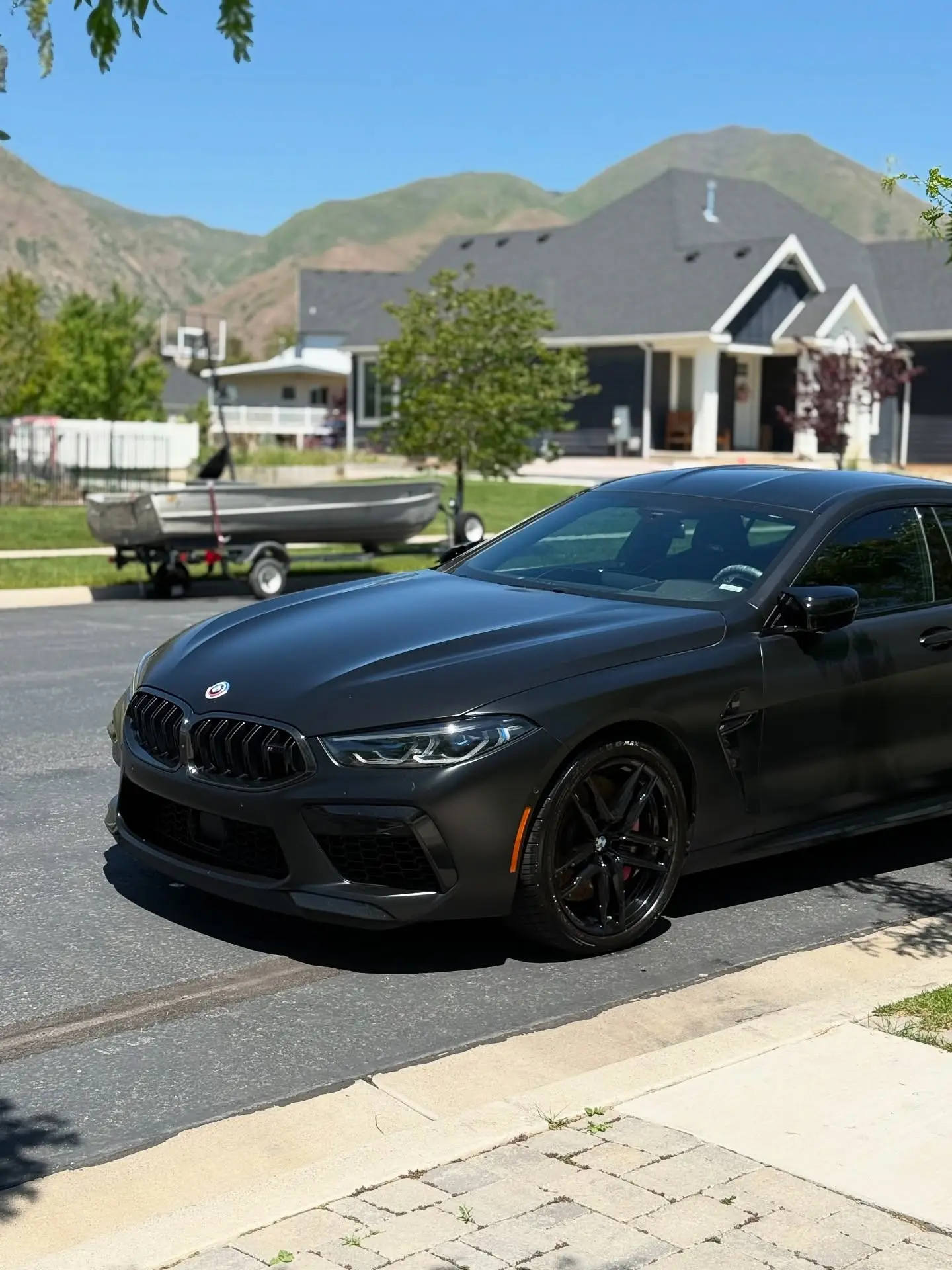 A matte black BMW M8 parked on a street below the Wasatch mountains