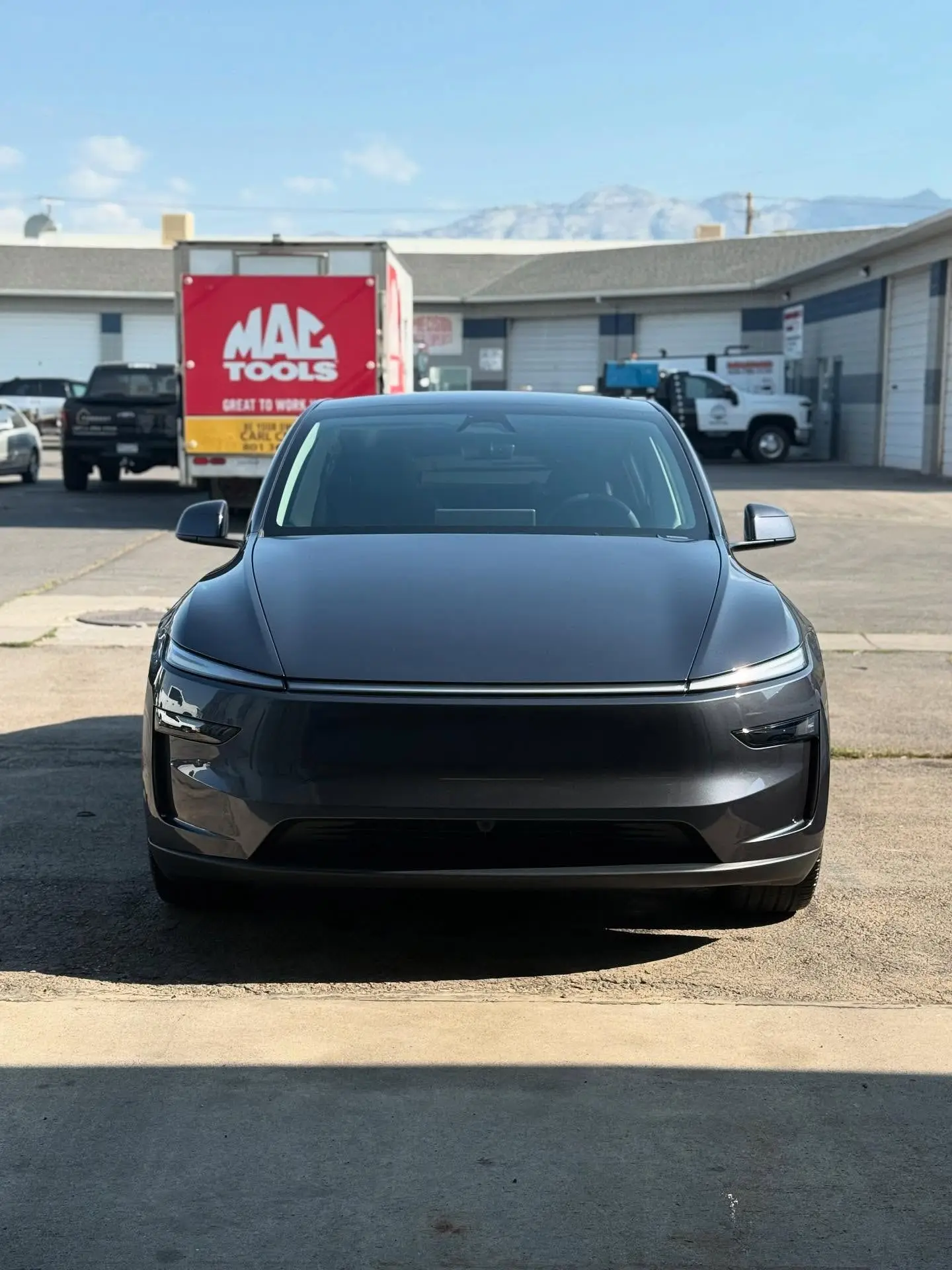 A gray Tesla Model Y parked front-on outside the shop with mountains behind