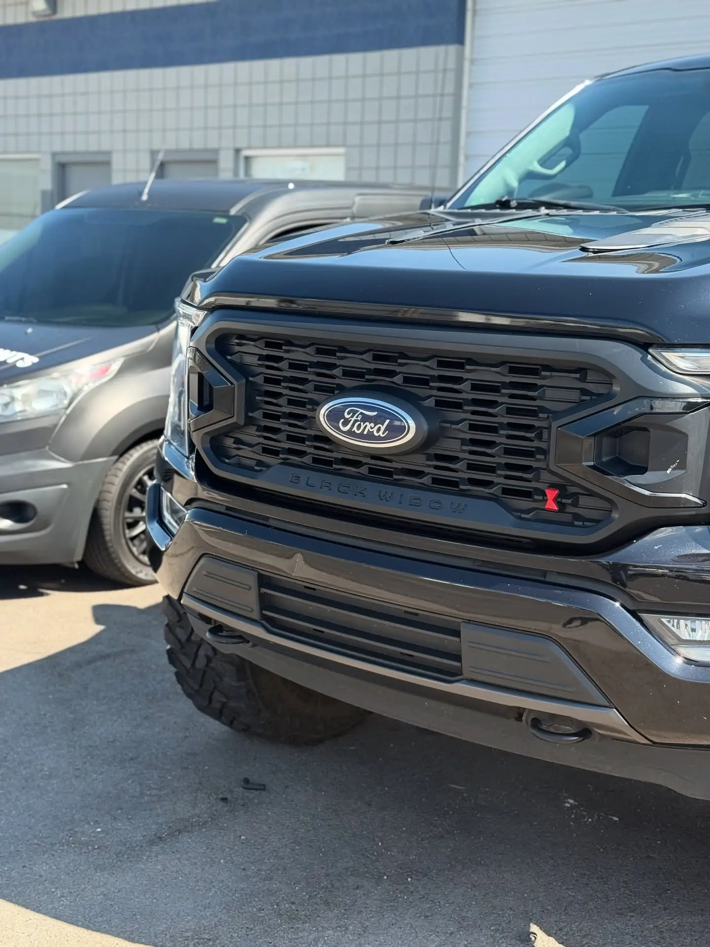 The front of a black lifted Ford F-150 outside the shop with mountains behind