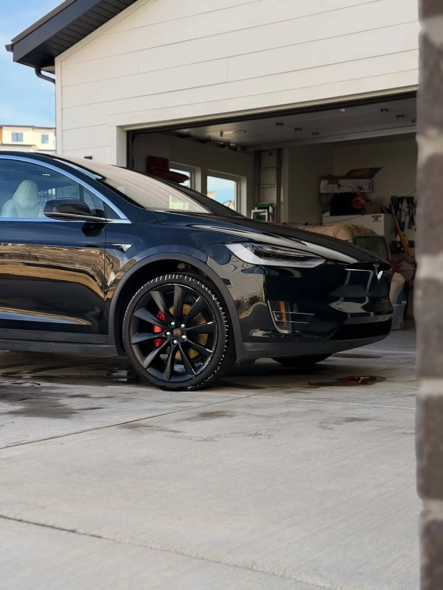 A black Tesla Model X on a driveway in front of an open garage