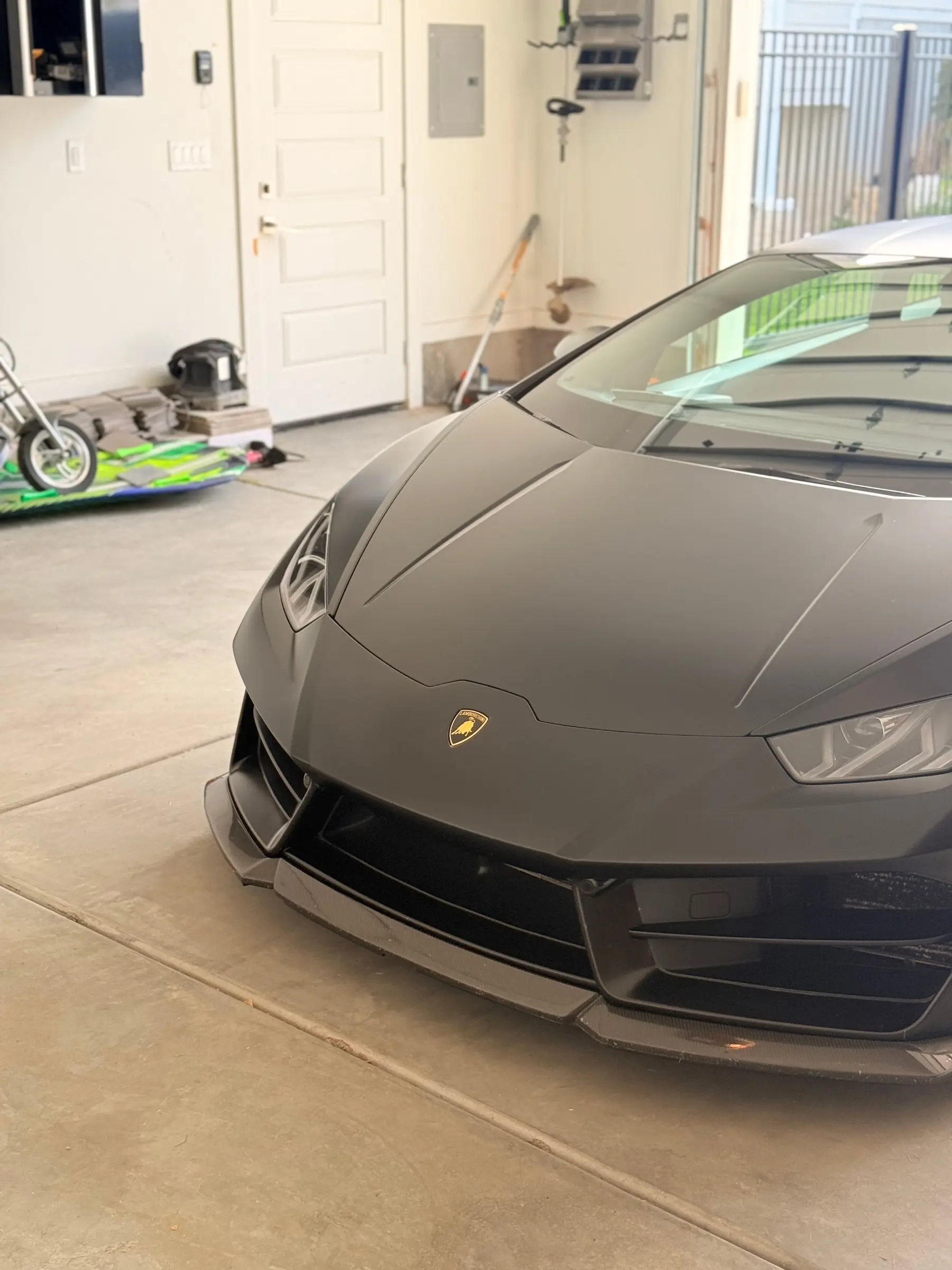 The nose of a matte black Lamborghini Huracán parked in a garage