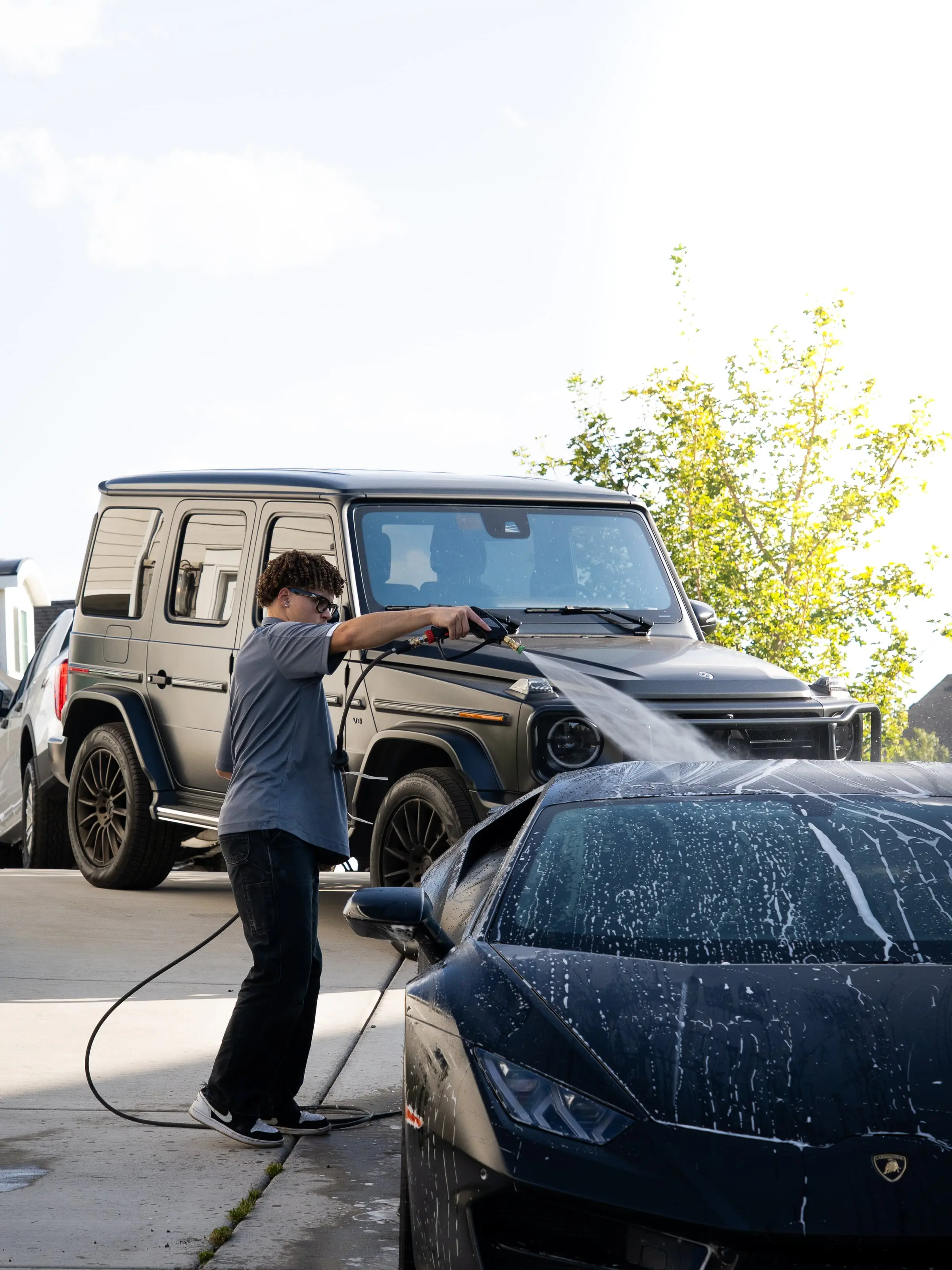 A technician rinsing a black Mercedes G-Wagon in a client driveway