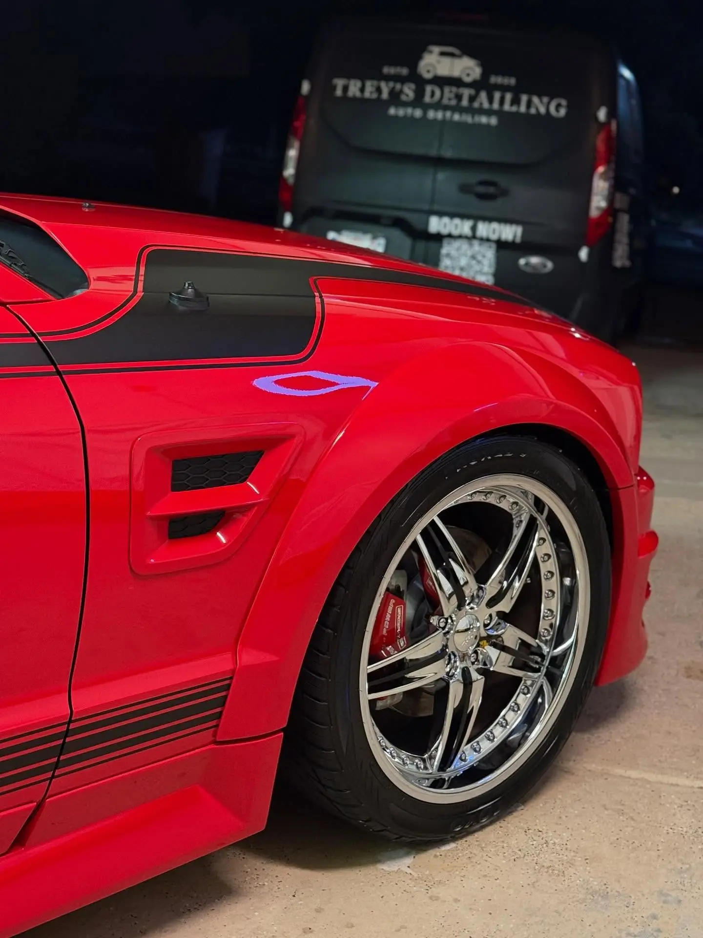 A red Mustang on chrome wheels with the Trey’s Detailing van parked behind it