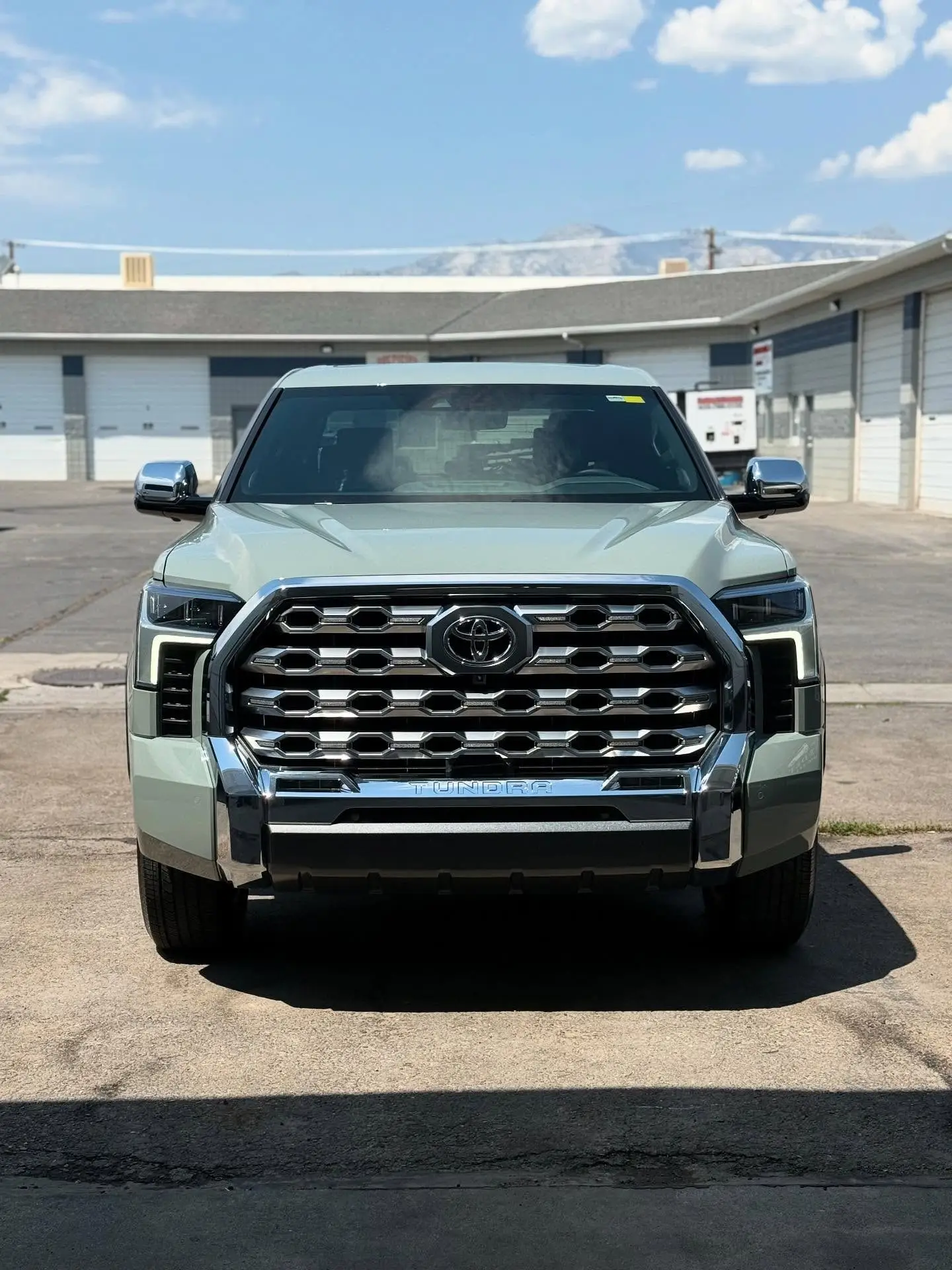 A sage green Toyota Tundra front-on outside the Bluffdale shop, mountains behind