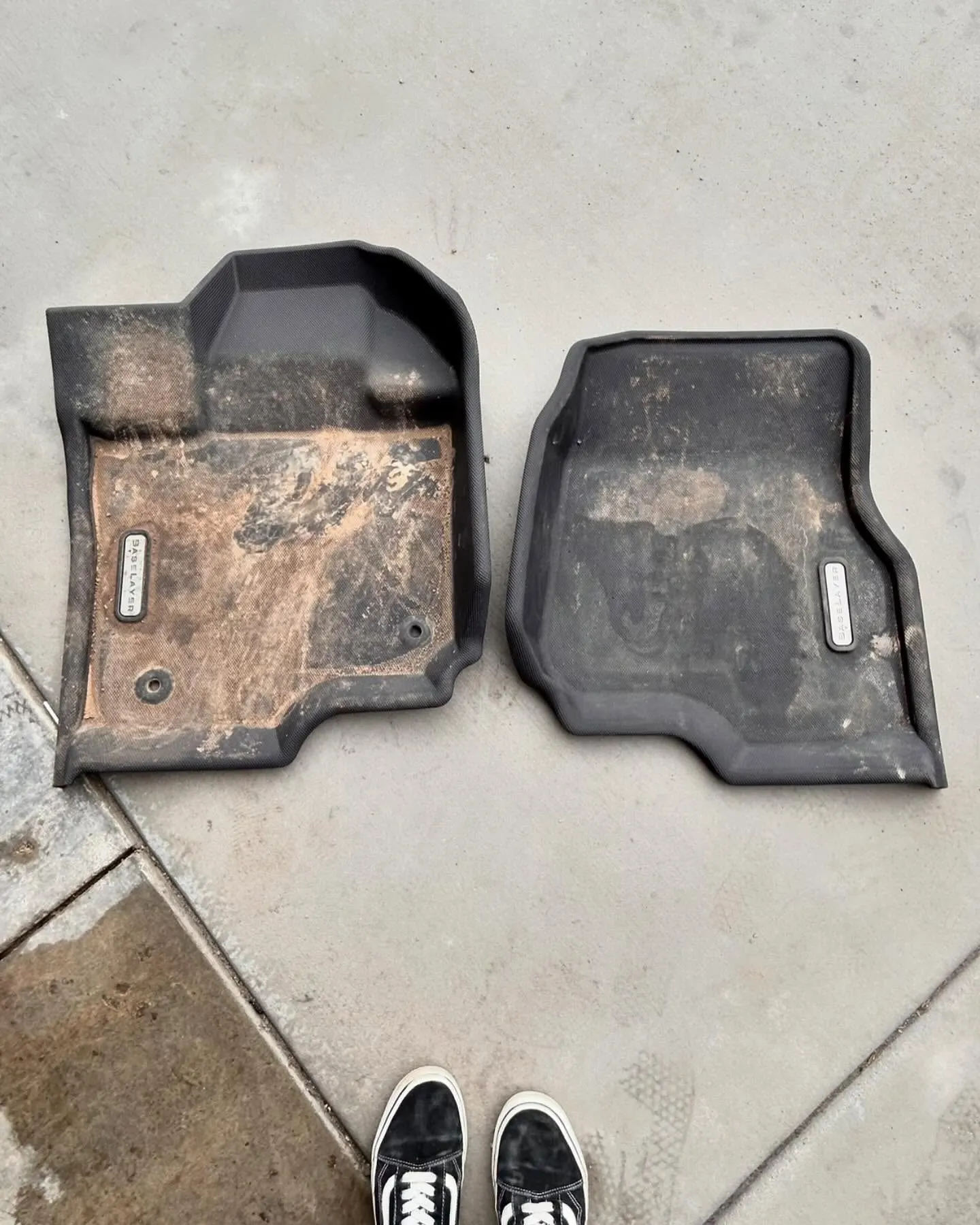A set of muddy floor mats on a driveway before a deep clean