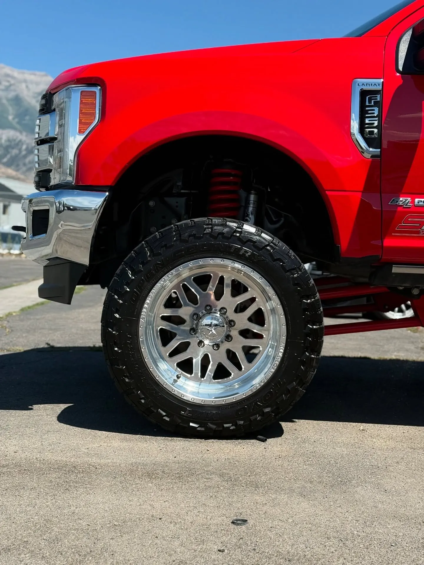 A lifted red Ford F-250 outside the shop with mountains behind