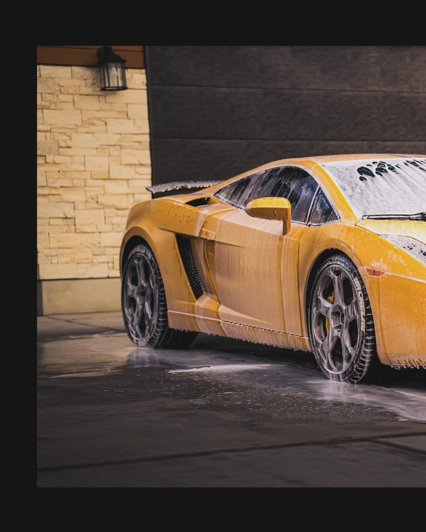 A technician washing a sudsy black Lamborghini Huracan low at the rocker